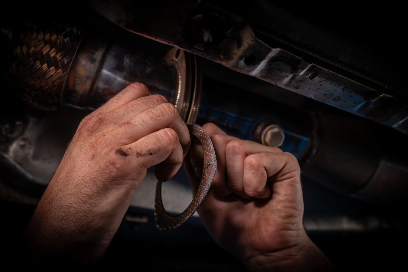 Mechanic's hands repairing an exhaust underneath a car on a hoist