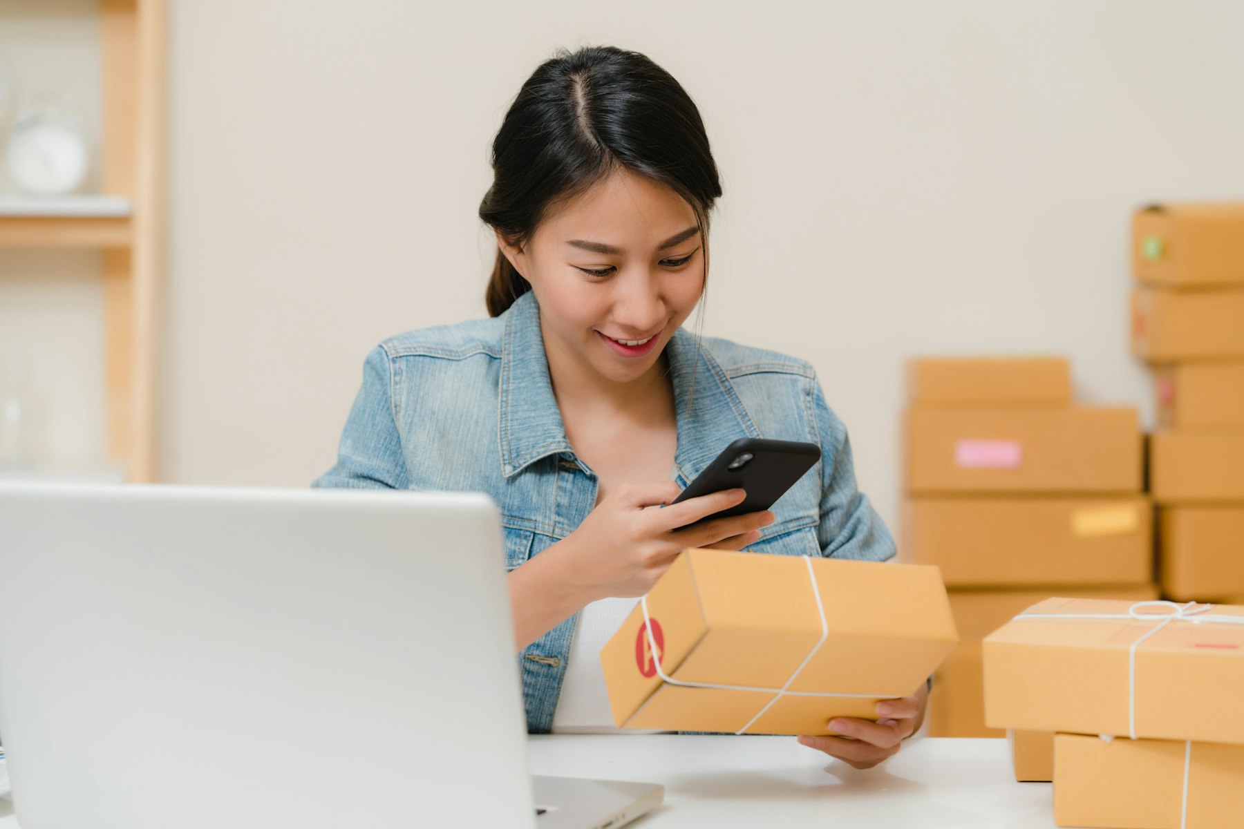 Online store owner checking an order on her phone while packing parcels