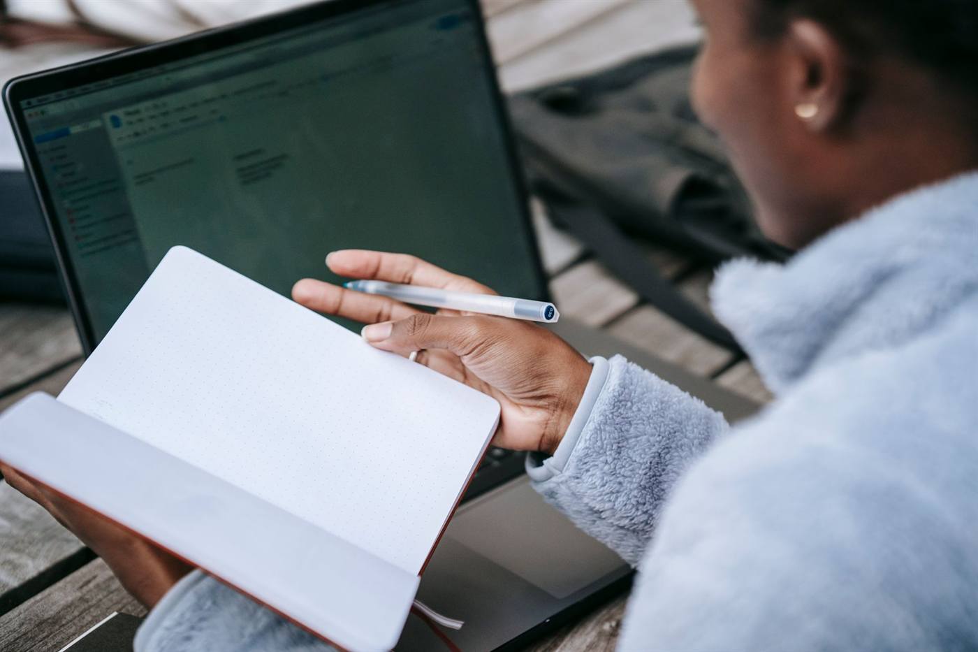 Student writing in a notebook beside an open laptop