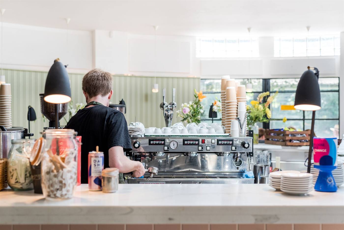 Barista working at an espresso machine behind the counter of a bright cafe