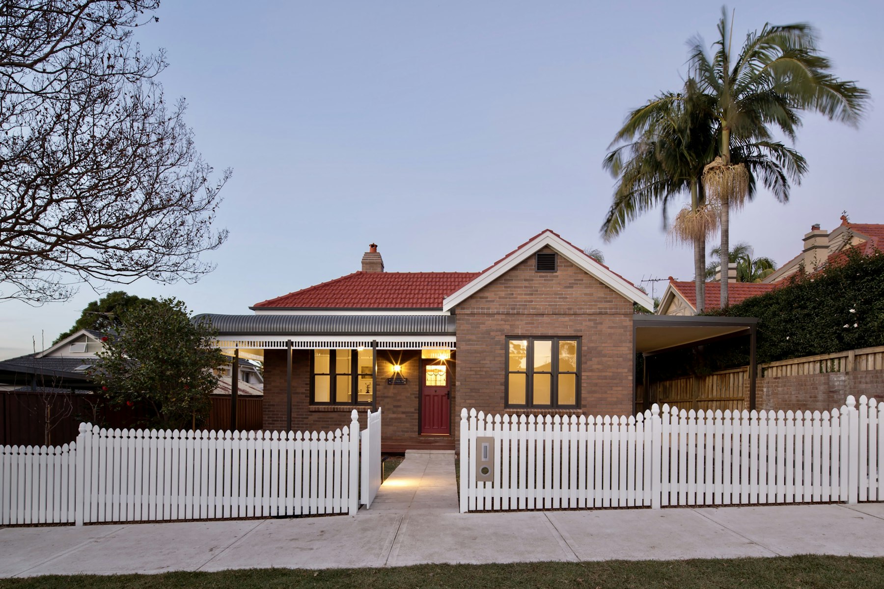 Renovated brick home behind a white picket fence at dusk in Chatswood, Sydney