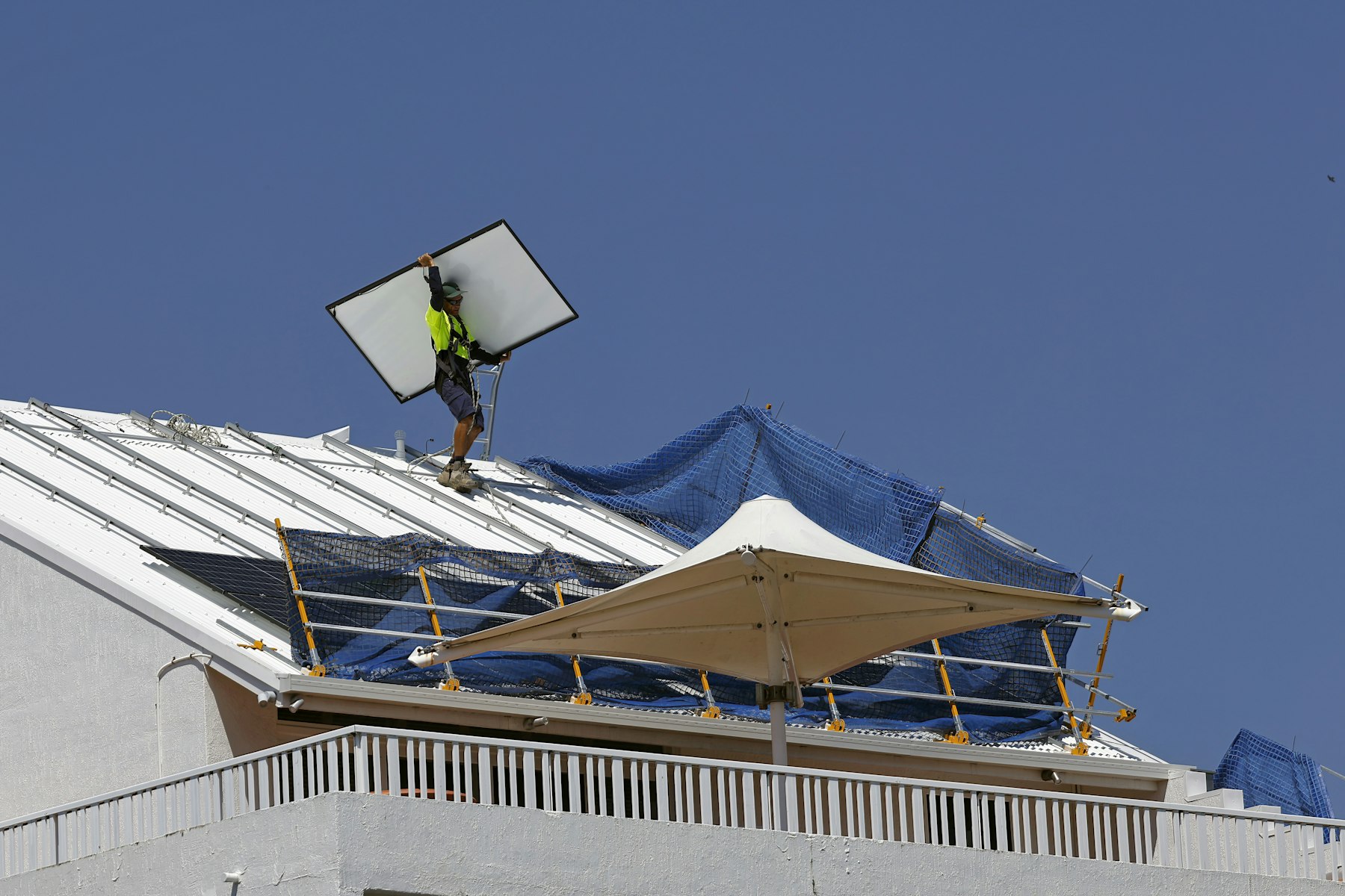 Solar installer carrying a panel across a rooftop under a clear blue sky in Cairns, Australia